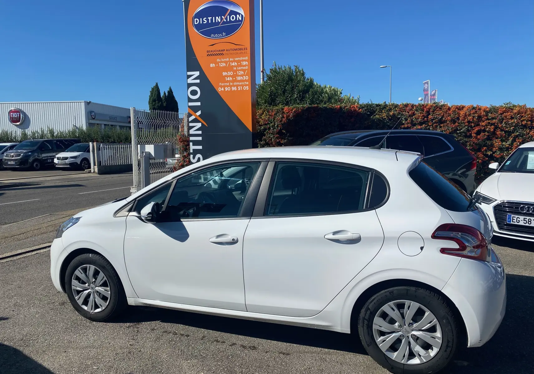 Vue latérale droite d'une Peugeot 208 blanche de 2014 garée devant un panneau Distinxion en extérieur.