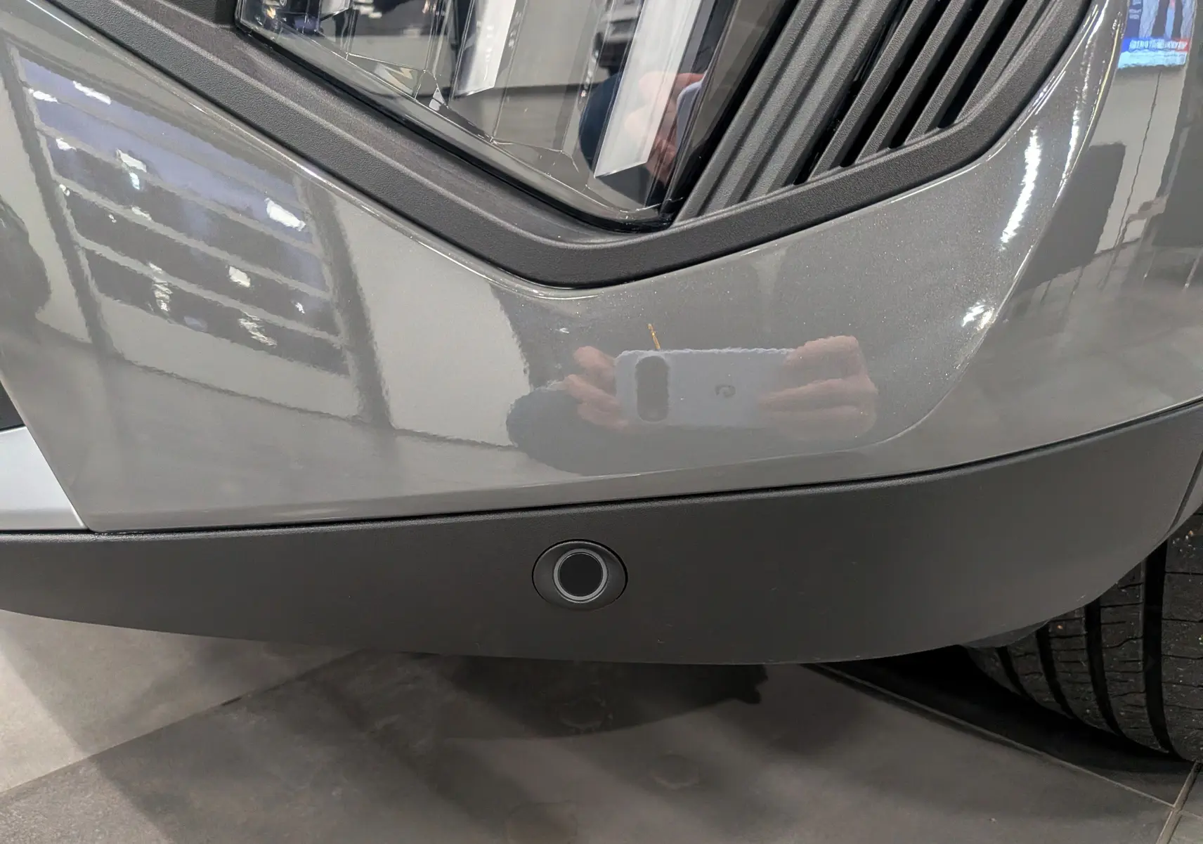 Gros plan sur le pare-chocs avant gris Sélénium du Peugeot 2008 Hybrid 145 e-DCS6 Allure avec capteur de stationnement visible.