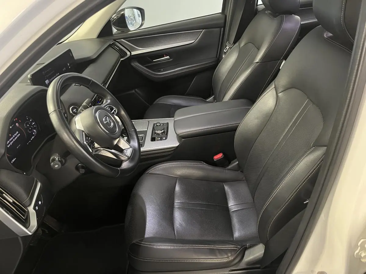 Intérieur du Mazda CX-60 blanc vu côté conducteur, sièges cuir noir avec surpiqûres bronze et tableau de bord moderne.