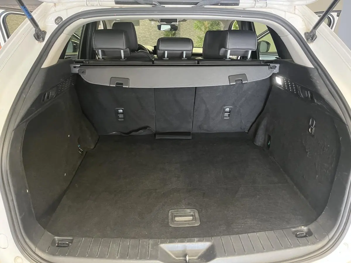 Coffre ouvert du Mazda CX-60 blanc 2023, vue arrière montrant l'espace de chargement et la plage arrière noire.