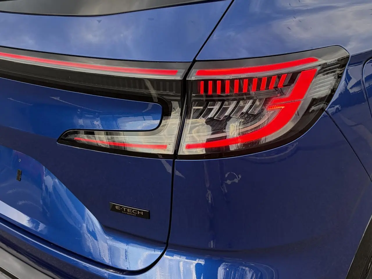 Gros plan sur le feu arrière droit rouge et noir du Renault Austral Bleu Iron avec logo E-Tech Hybrid visible.