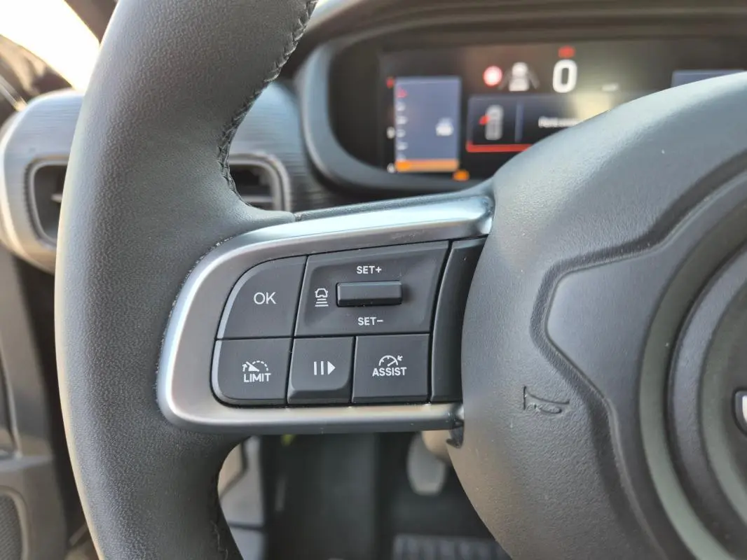 Gros plan sur les commandes au volant côté gauche du Jeep Avenger noir 2024, avec affichage numérique en arrière-plan.