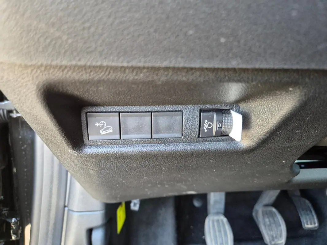 Gros plan sur les commandes de régulateur de vitesse et réglage des phares sous le tableau de bord côté conducteur du Jeep Avenger noir.