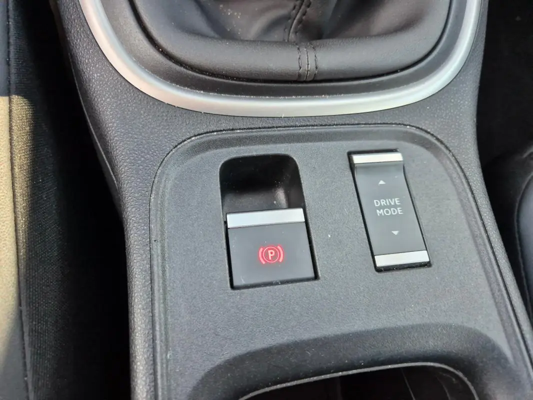 Gros plan sur la console centrale noire du Jeep Avenger 2024 montrant le frein à main électrique et le bouton Drive Mode.