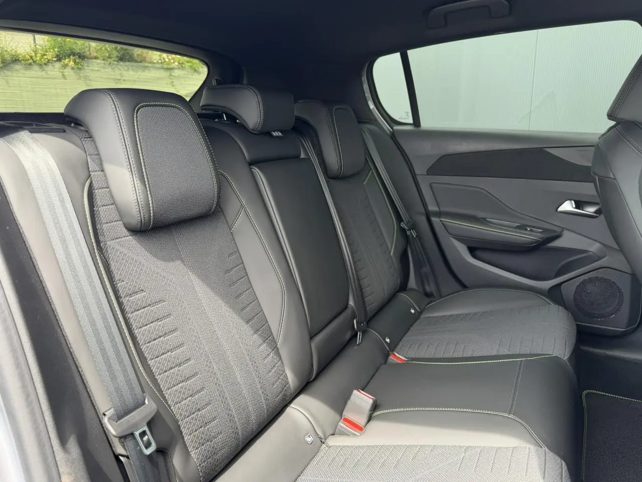 Vue intérieure des sièges arrière noirs avec surpiqûres vertes de la Peugeot 308 NV Hybrid 145 GT e-DSC6 2026.