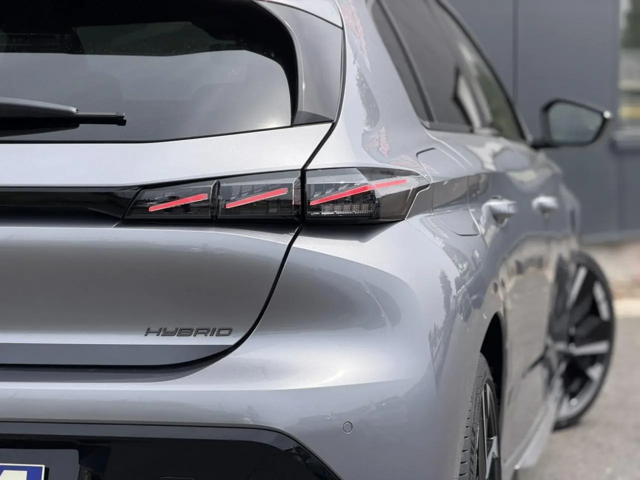 Vue 3/4 arrière droite d'une Peugeot 308 Hybrid gris Artense avec feux arrière LED à trois griffes et jantes bi-ton.