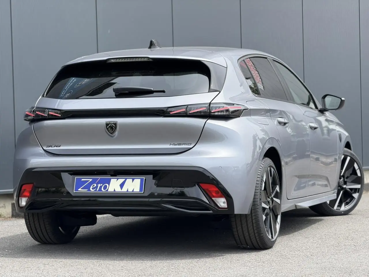 Vue 3/4 arrière droite d'une Peugeot 308 NV Hybrid 145 GT gris Artense avec jantes alliage bi-tons et feux arrière LED 3 griffes.