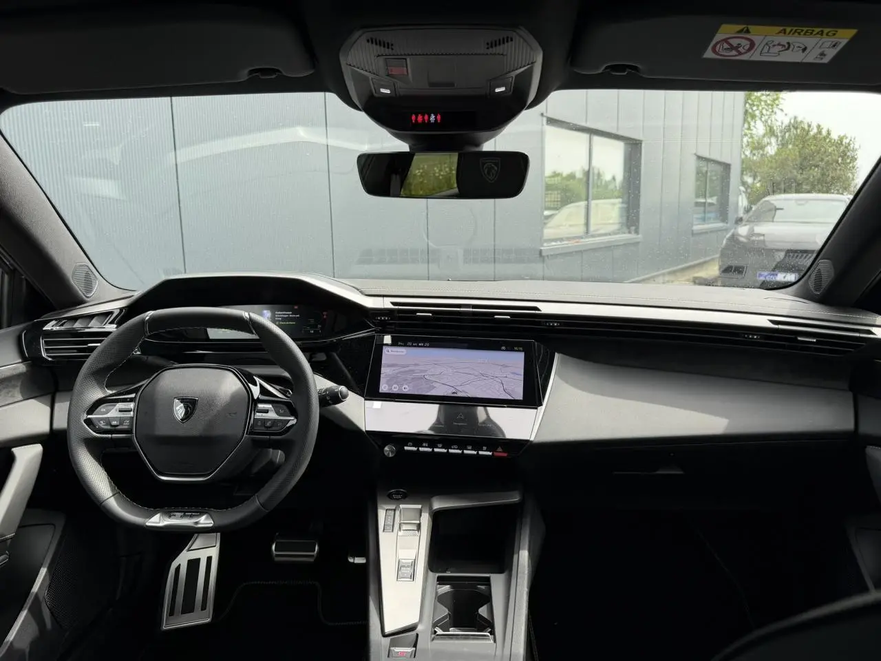 Vue intérieure avant du Peugeot 308 gris Artense, mettant en valeur le volant compact GT, l'écran tactile central et le combiné numérique.