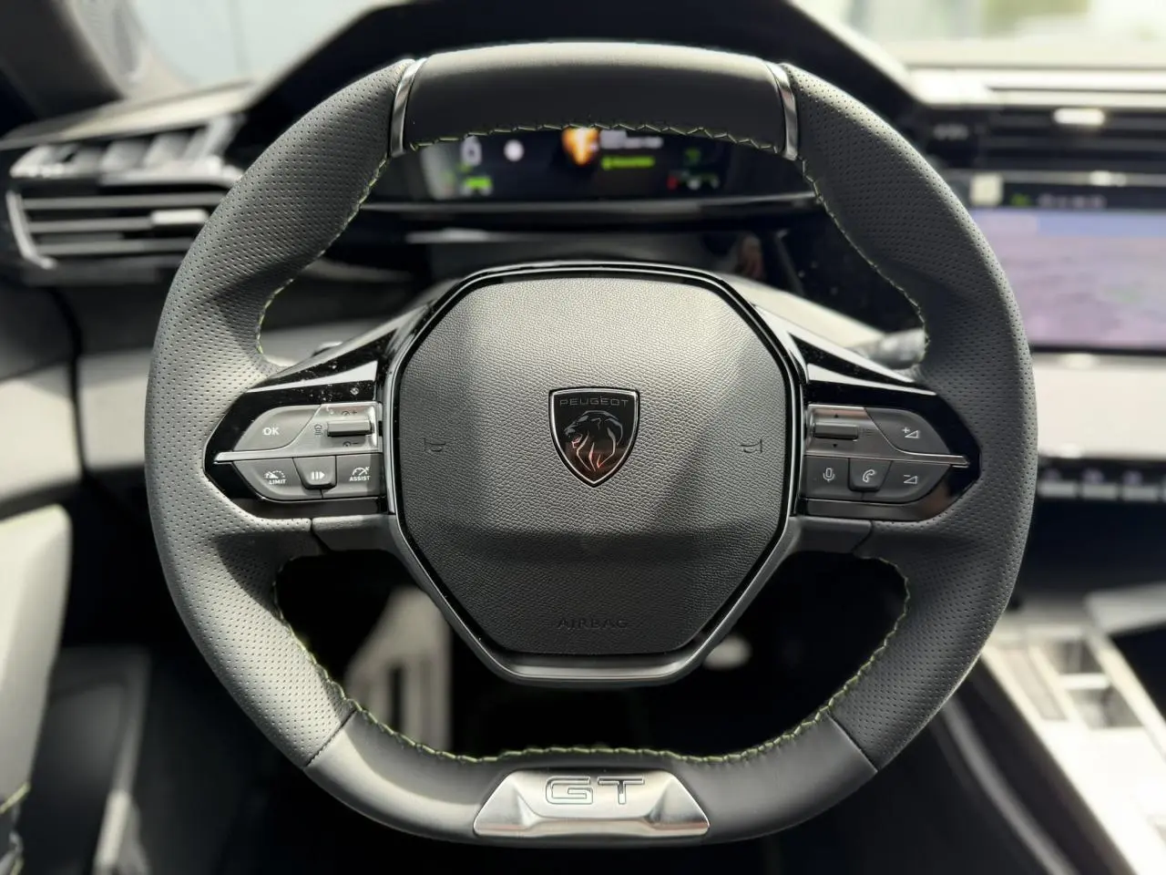 Volant compact GT en cuir noir avec surpiqûres vert Adamite et logo Peugeot, vue frontale centrée sur le volant.