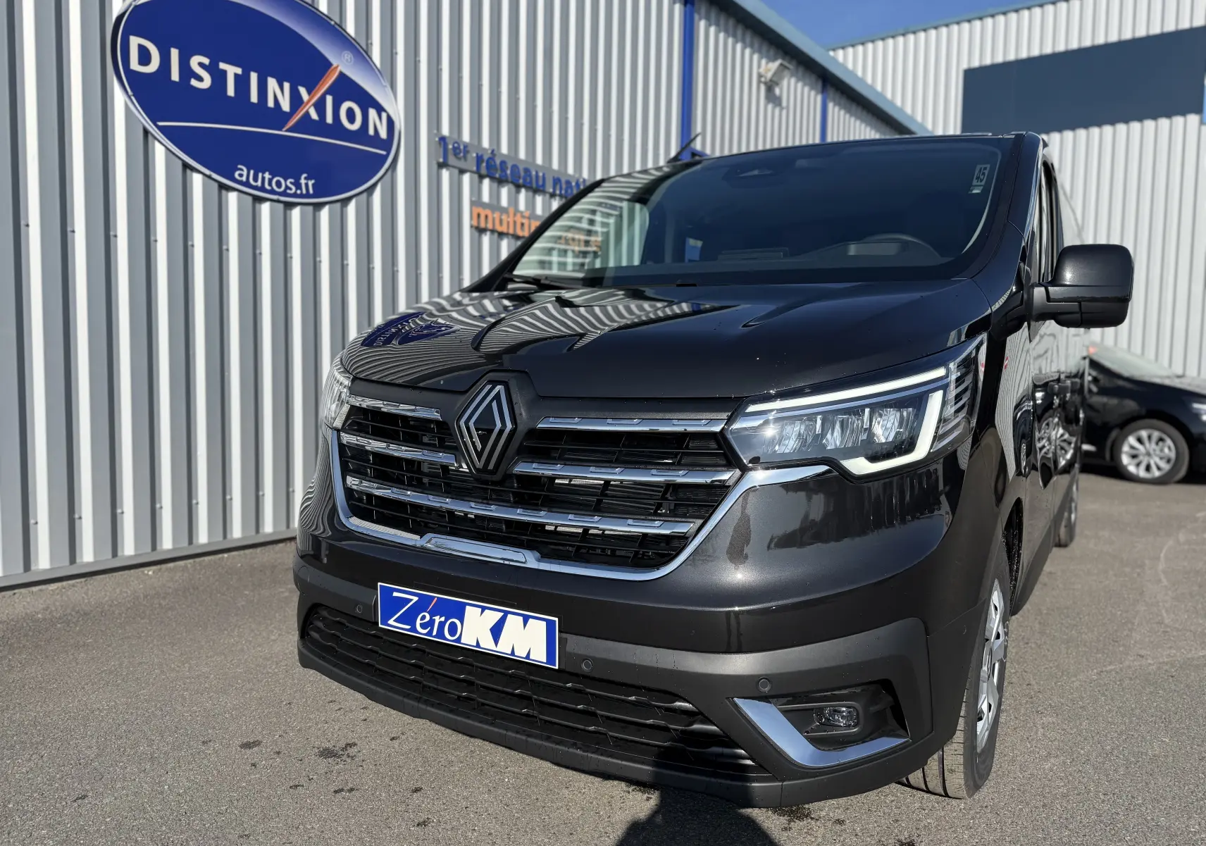 Vue 3/4 avant droit du Renault Trafic cabine approfondie noir, avec calandre chromée et phares LED allumés.