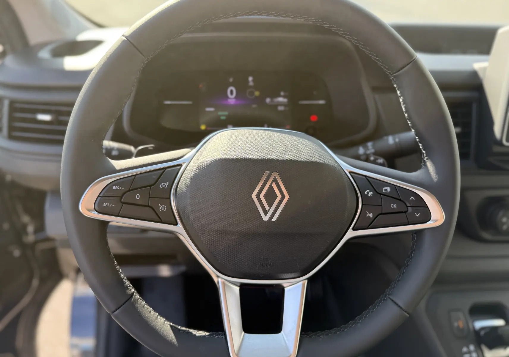 Vue rapprochée du volant noir du Renault Trafic L2H1 2025, avec commandes intégrées et logo central argenté.