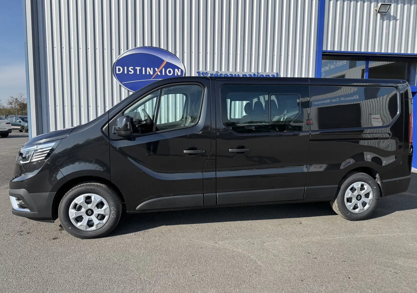 Profil côté gauche d’un Renault Trafic Cabine Approfondie noir 2025, stationné devant un bâtiment commercial.