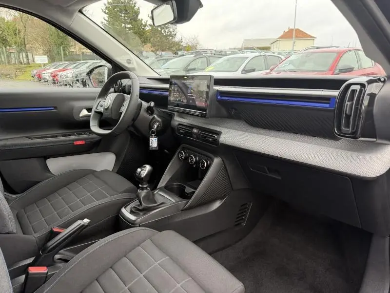 Intérieur avant droit de la Citroën C3 2025 avec tableau de bord noir, écran tactile et détails bleus lumineux.