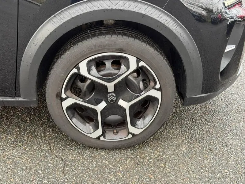 Gros plan sur la roue avant gauche noire avec jante spécifique bicolore du Citroën C3 1.2 Turbo 100ch PLUS 2025.