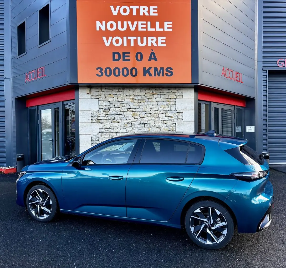 Peugeot 308 Hybrid 136 e-DCS6 Allure bleu vue de profil côté gauche devant un bâtiment avec panneau orange "Votre nouvelle voiture".