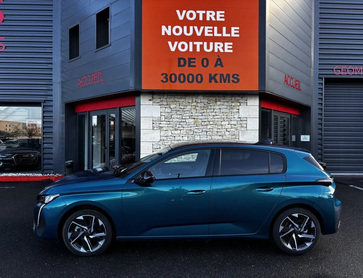 Profil côté gauche d'une Peugeot 308 Hybrid 136 e-DCS6 Allure bleu métallisé, garée devant un bâtiment avec panneau orange.