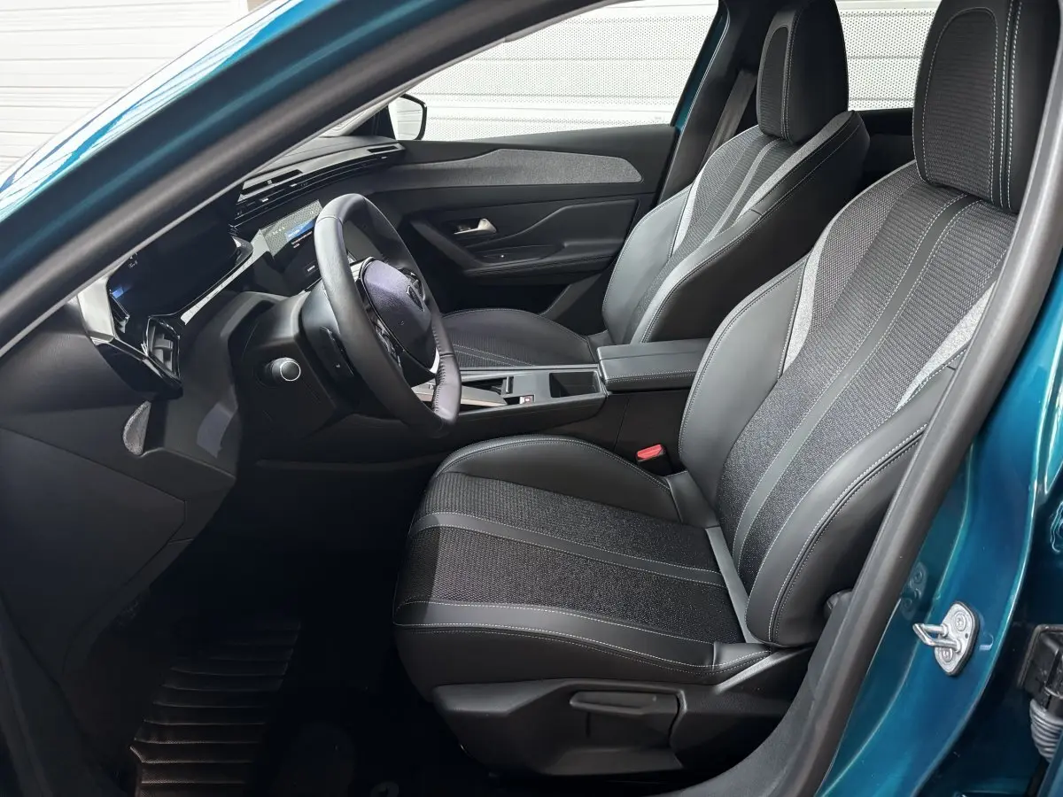 Vue intérieure côté conducteur de la Peugeot 308 Hybrid bleu, avec sièges tissu et cuir et volant multifonctions cuir.
