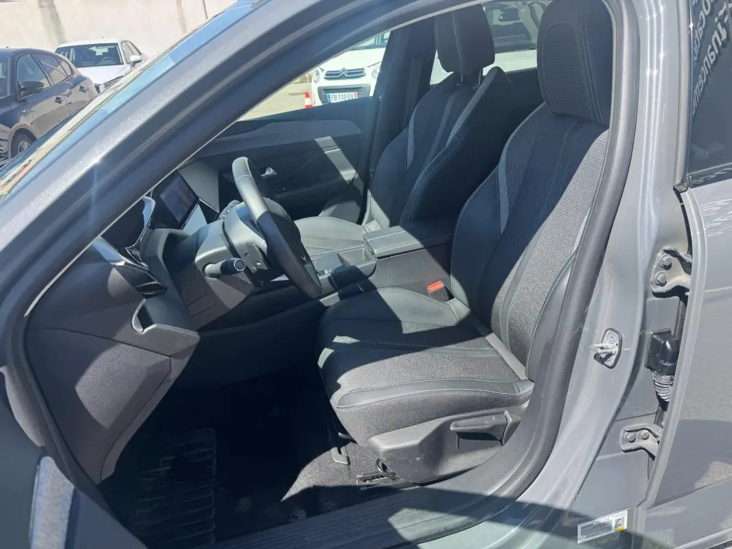 Intérieur avant droit de la Peugeot 308 Hybrid gris 2025, sièges tissu avec accoudoir central et tableau de bord moderne.