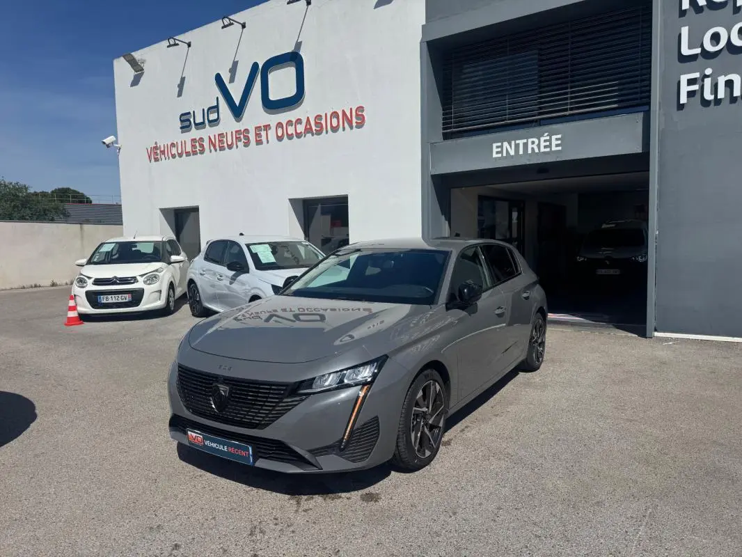 Peugeot 308 Hybrid gris vue 3/4 avant droit, jantes alliage 17 pouces, stationnée devant un garage Sud VO.