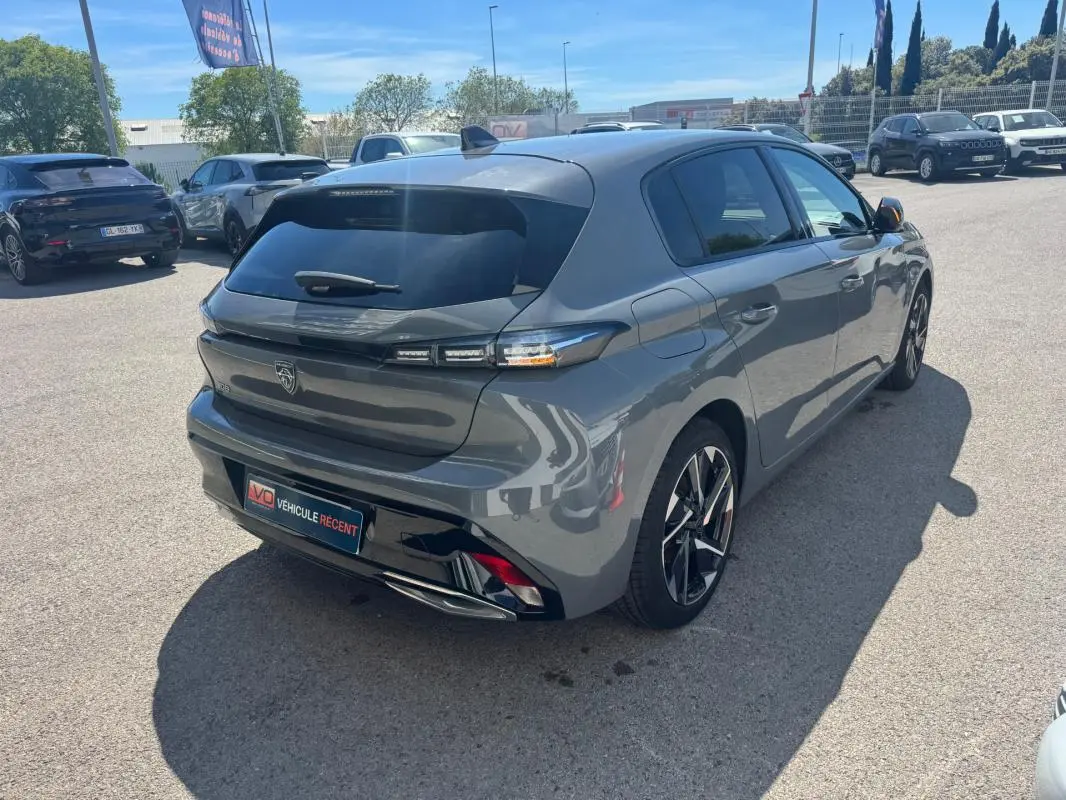 Vue 3/4 arrière droite d'une Peugeot 308 Hybrid gris métallisé avec jantes alliage 17 pouces sur parking.