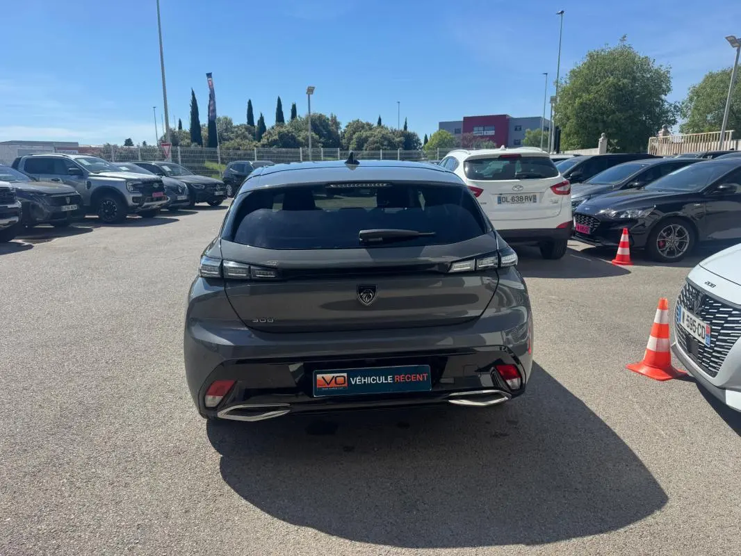 Vue arrière d'une Peugeot 308 Hybrid gris foncé stationnée en extérieur, avec feux arrière LED et double sortie d'échappement intégrée.