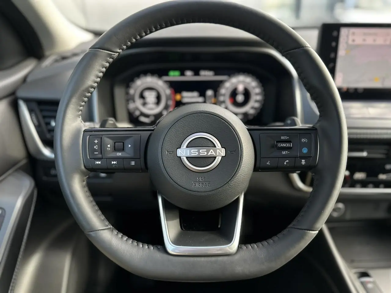 Volant cuir noir de Nissan Qashqai 2025 vu de face avec commandes intégrées et tableau de bord numérique flou en arrière-plan.