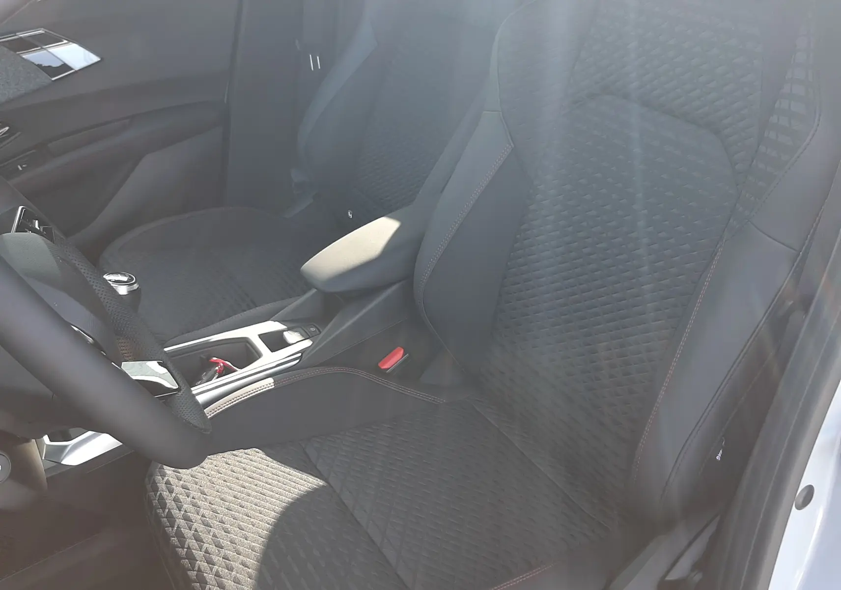 Vue intérieure côté conducteur de la Renault Clio VI TCe 115ch Techno, sièges noirs avec surpiqûres rouges et console centrale.