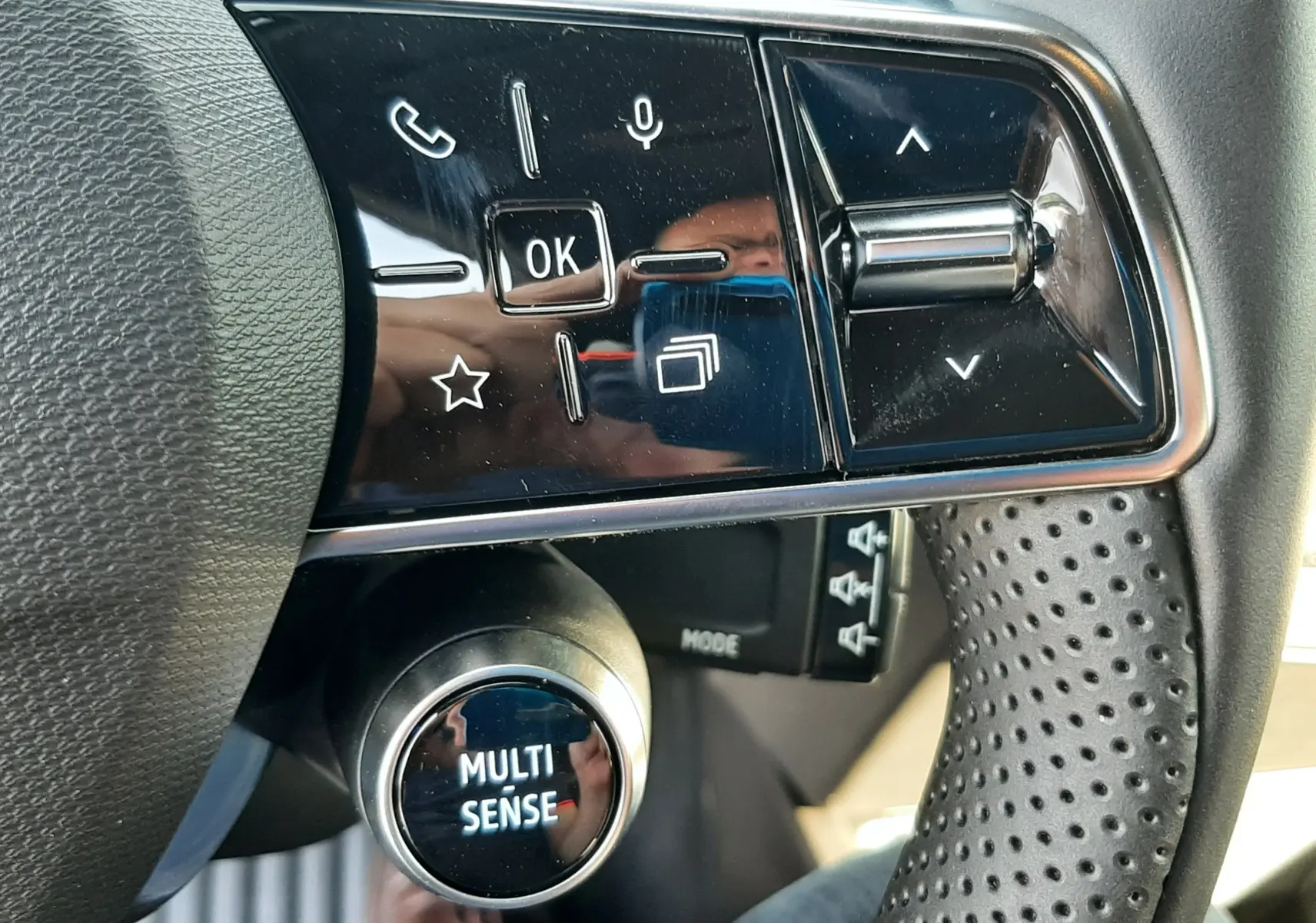 Gros plan sur les commandes multifonctions noires et brillantes du volant perforé côté gauche de la Renault Clio VI Gris Rafale.