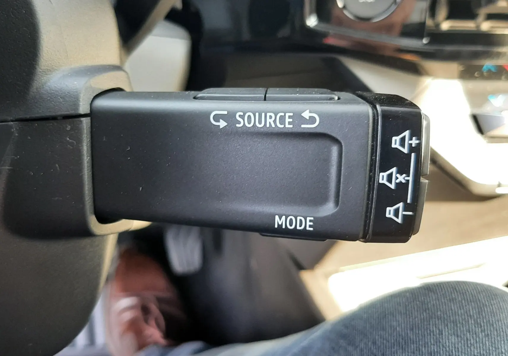 Gros plan sur la commande au volant droite de la Renault Clio VI gris Rafale, avec boutons source et mode visibles.