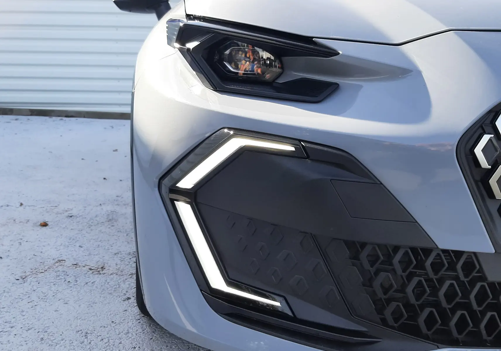 Gros plan sur l'avant gauche de la Renault Clio VI gris Rafale, mettant en valeur le phare et la signature lumineuse LED en forme de C.