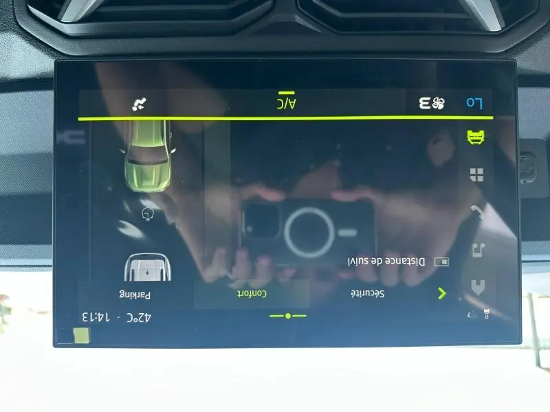 Écran tactile central du Dacia Duster blanc 2025 montrant les réglages climatisation et assistance au stationnement.