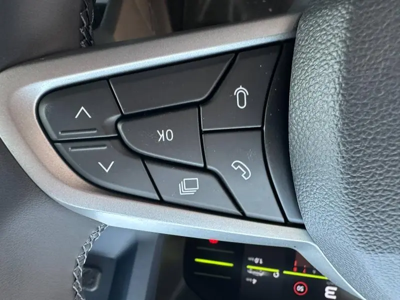 Gros plan sur les commandes noires multifonctions au volant du Dacia Duster blanc, avec coutures visibles sur le cuir.