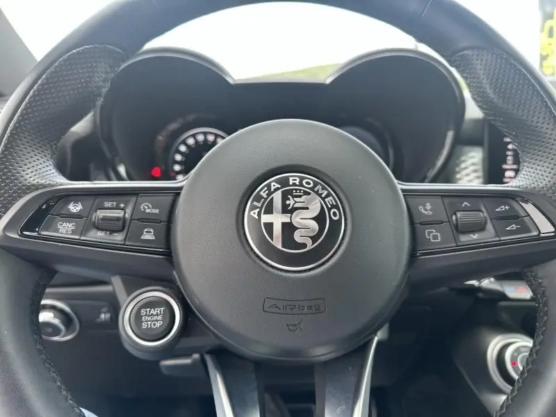 Gros plan sur le volant cuir de l'Alfa Romeo Tonale 2024 avec logo central et commandes intégrées, intérieur noir.