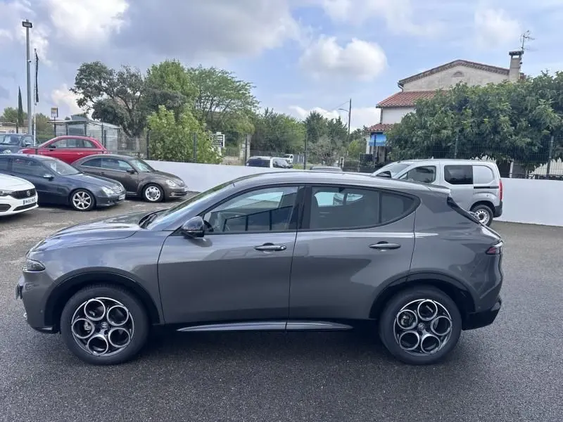 Profil côté gauche de l'Alfa Romeo Tonale 1.5 Hybrid gris foncé métal avec jantes distinctives en cercle, sur parking extérieur.