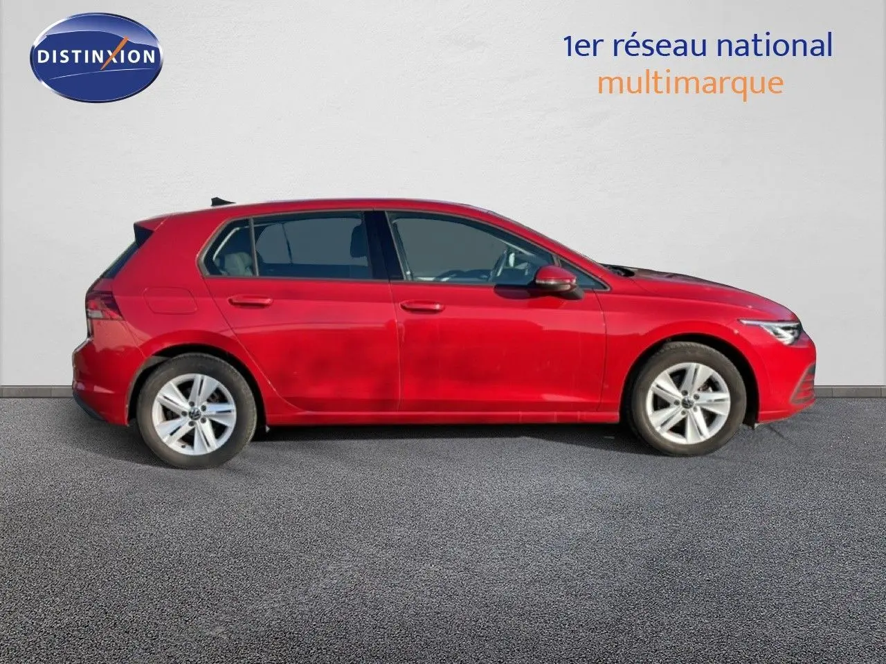 Profil droit d'une Volkswagen Golf VIII rouge roi métal, avec jantes alliage et vitres teintées, sur fond clair.