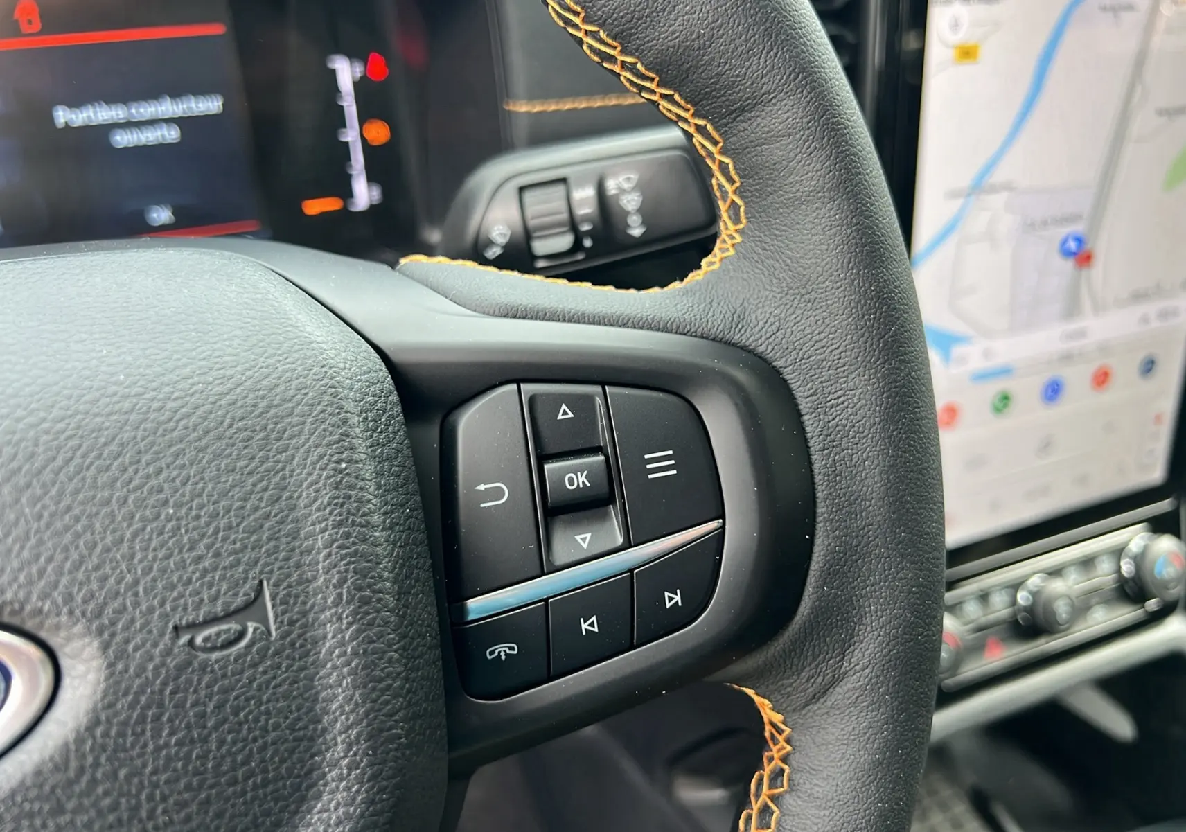 Gros plan sur le volant cuir noir avec surpiqûres orange du Ford Ranger 2026, boutons multifonctions et écran tactile GPS visible.