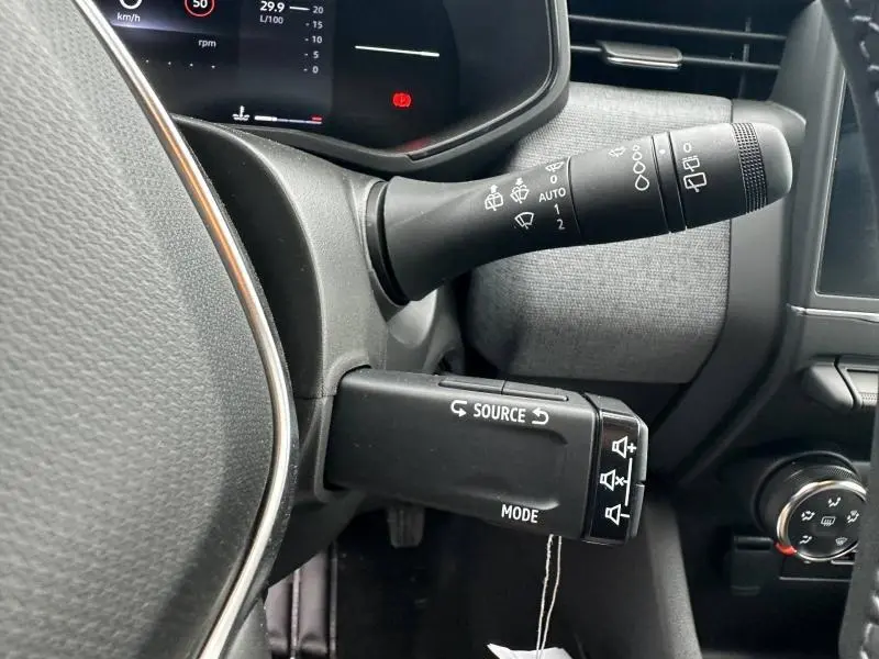 Gros plan sur les commandes au volant côté gauche de la Renault Clio gris Rafale, avec levier d’essuie-glace et commandes audio.