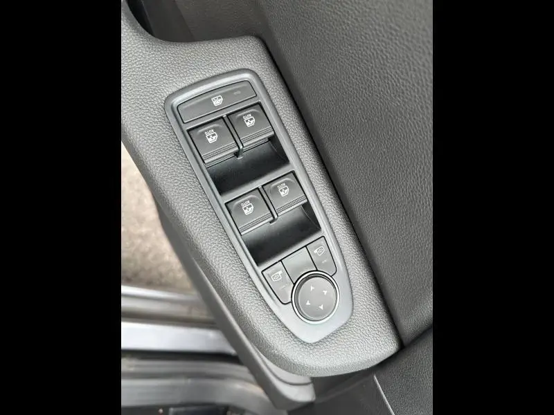 Gros plan sur les commandes des vitres électriques et réglages des rétroviseurs côté conducteur de la Renault Clio gris Rafale.