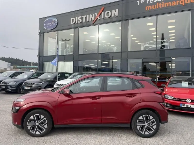 Vue de profil côté gauche d'un Hyundai Kona électrique rouge métal 2021 garé devant un showroom Distinxion.