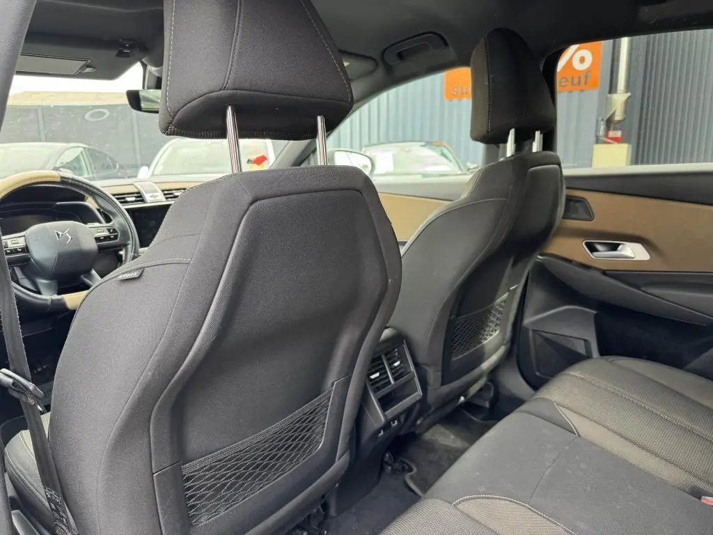 Vue intérieure arrière du DS7 Crossback gris, montrant les sièges avant en tissu noir et les aérateurs centraux.