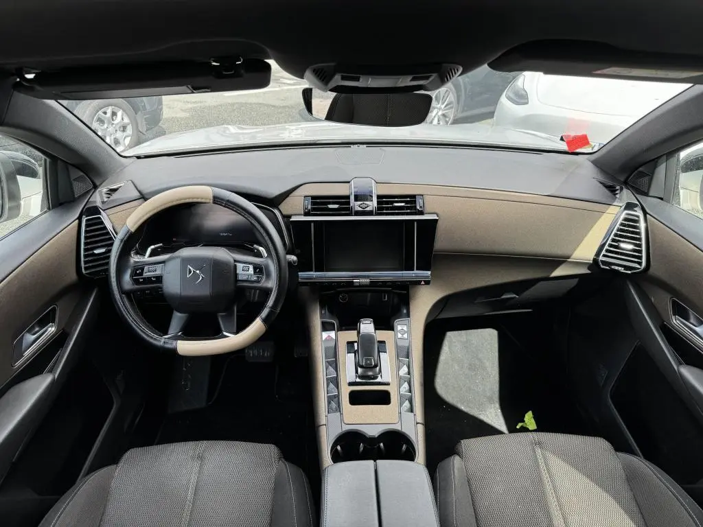 Vue intérieure avant du DS7 Crossback 2022 avec tableau de bord beige et noir, volant bicolore et écran tactile central.