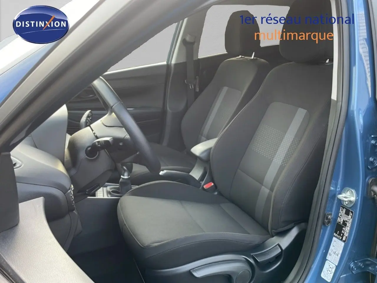 Vue intérieure côté conducteur de la Hyundai i20 2025 bleu vibrant metal, montrant les sièges noirs et le volant.