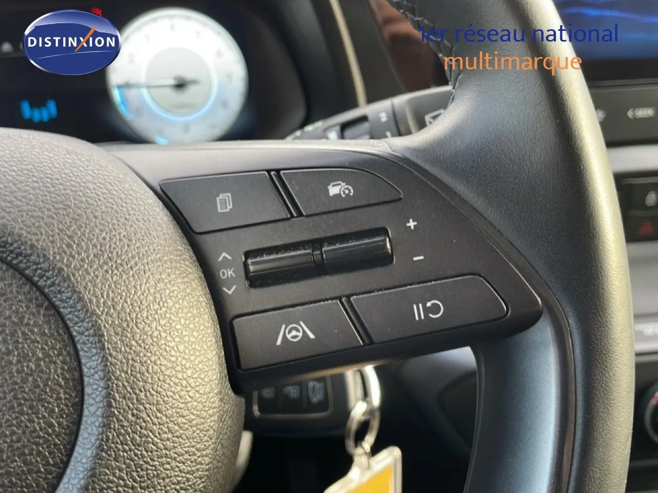 Gros plan sur le volant côté droit d'une Hyundai i20 2025, avec commandes de régulateur et tableau de bord flou en arrière-plan.