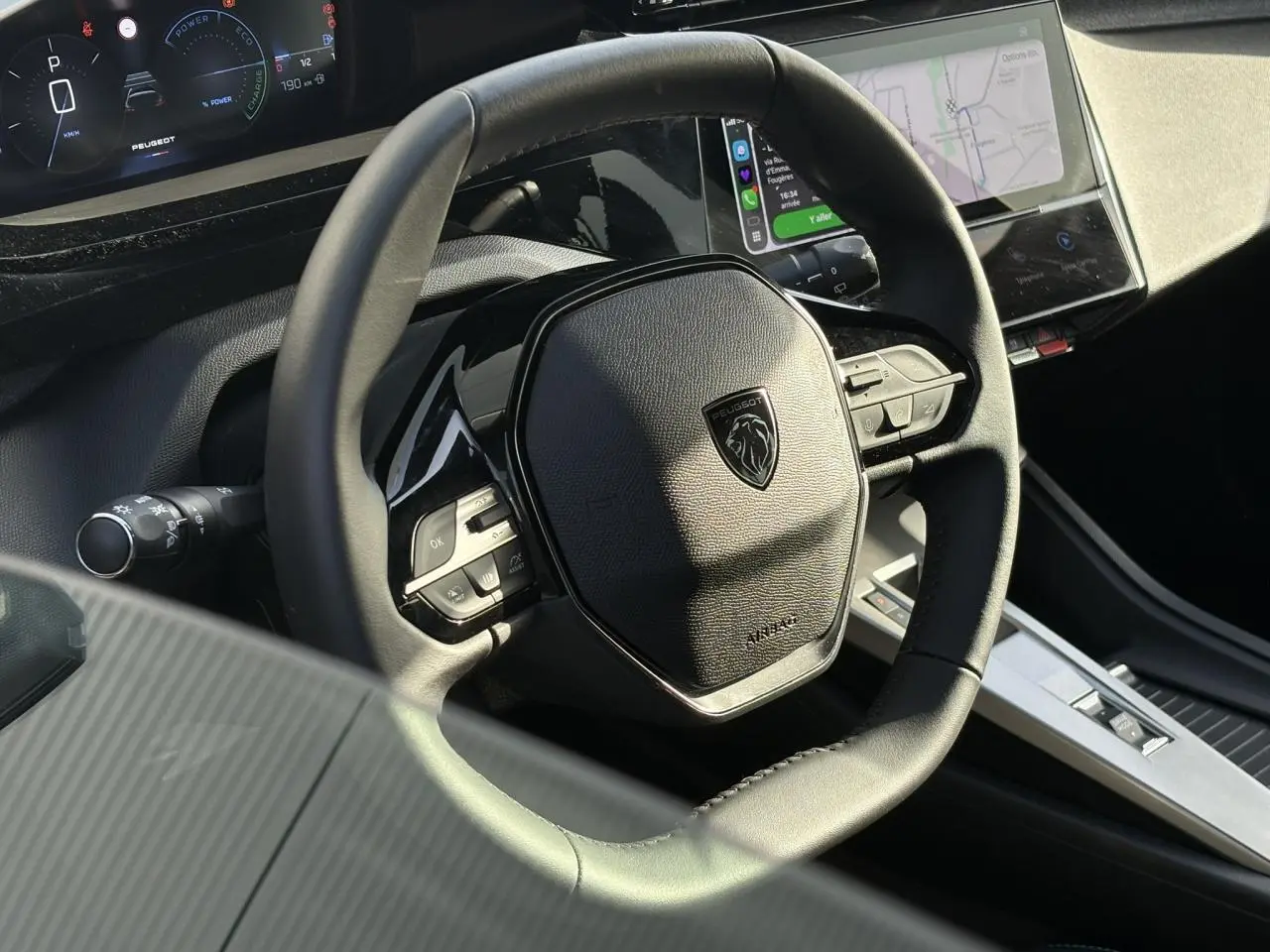 Vue rapprochée du volant cuir noir de la Peugeot 308 Hybrid 2025 avec tableau de bord numérique et écran tactile.