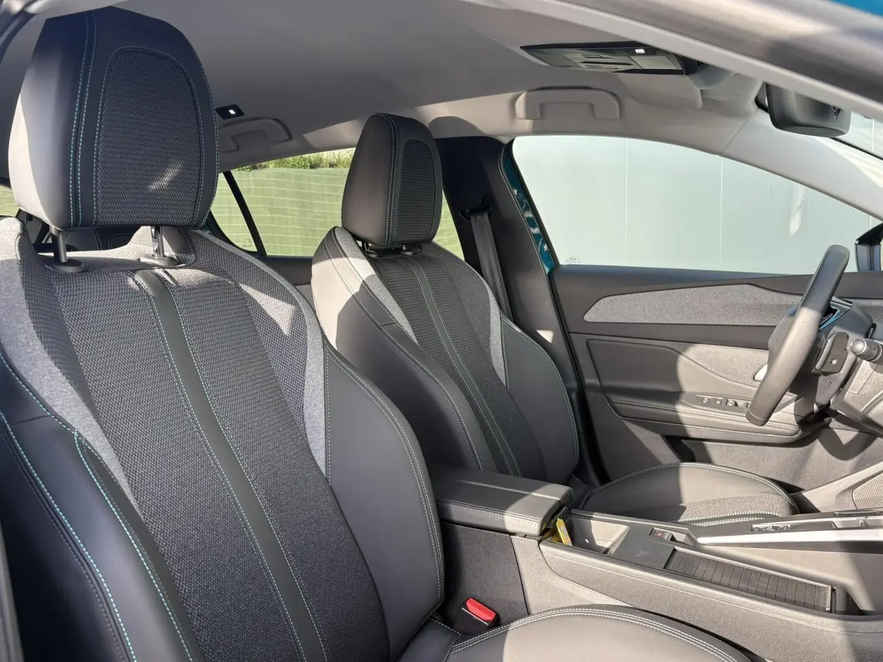 Vue intérieure côté conducteur de la Peugeot 308 Hybrid 145 Allure avec sièges tissu et cuir noirs et surpiqûres bleues.