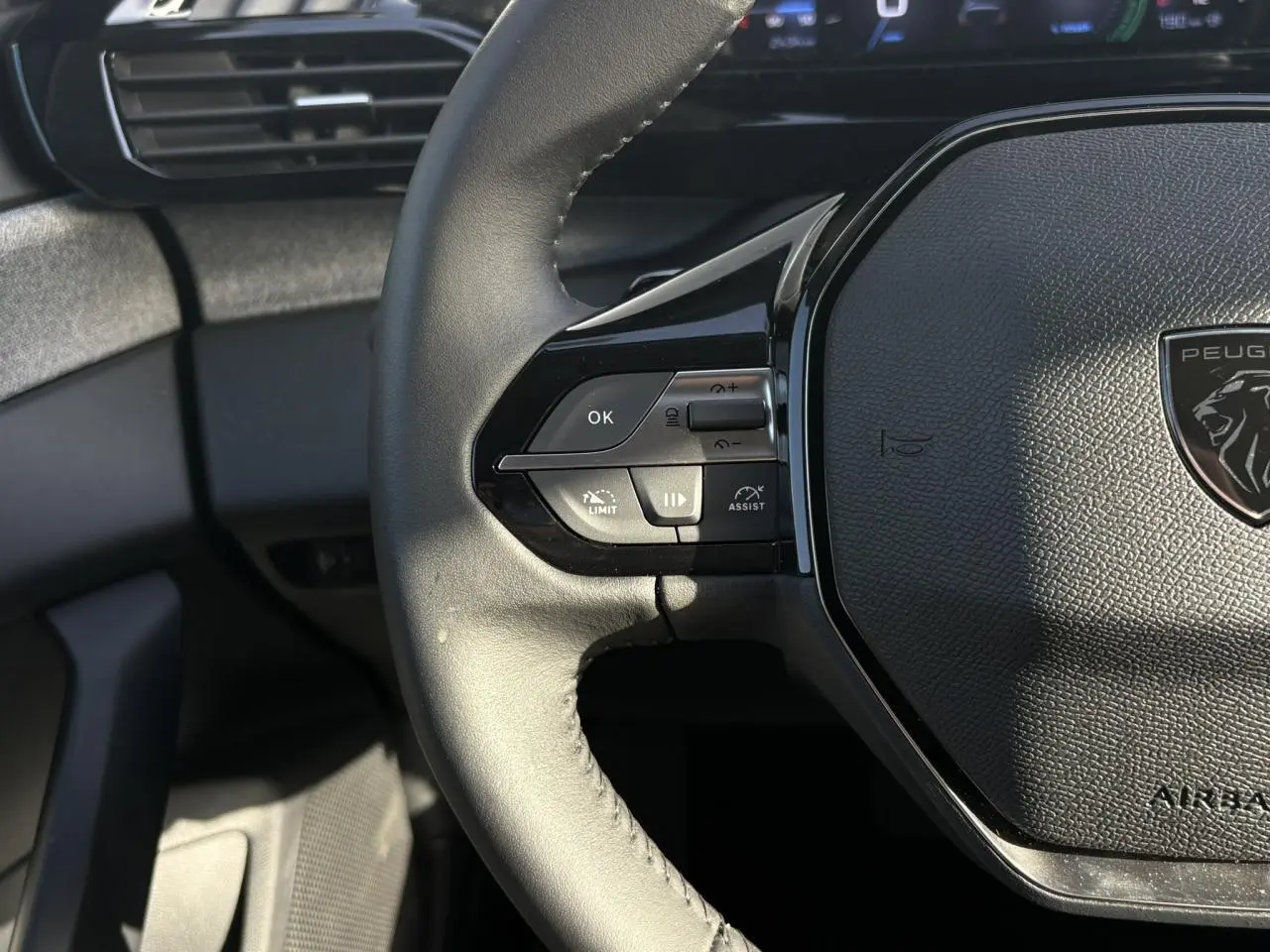 Gros plan sur le volant cuir noir de la Peugeot 308 Hybrid 2025, avec commandes intégrées et logo lion central.
