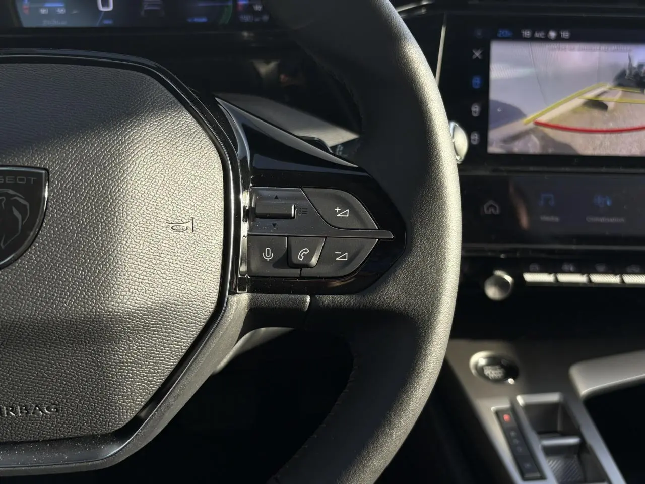Gros plan sur le volant en cuir noir de la Peugeot 308 Hybrid 2025 avec commandes intégrées et écran tactile affichant la caméra 360°.