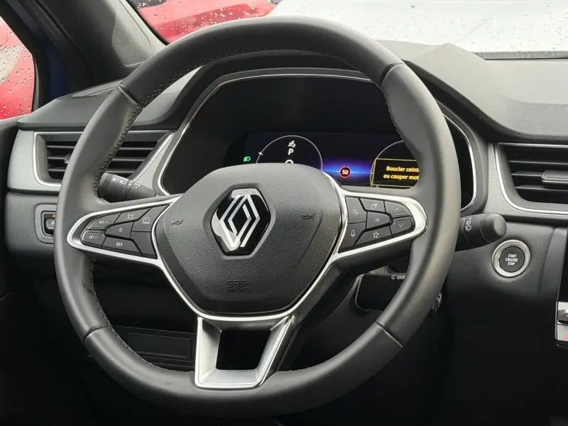 Vue rapprochée du volant multifonction noir du Renault Captur 2025 avec tableau de bord digital et bouton start/stop visible.