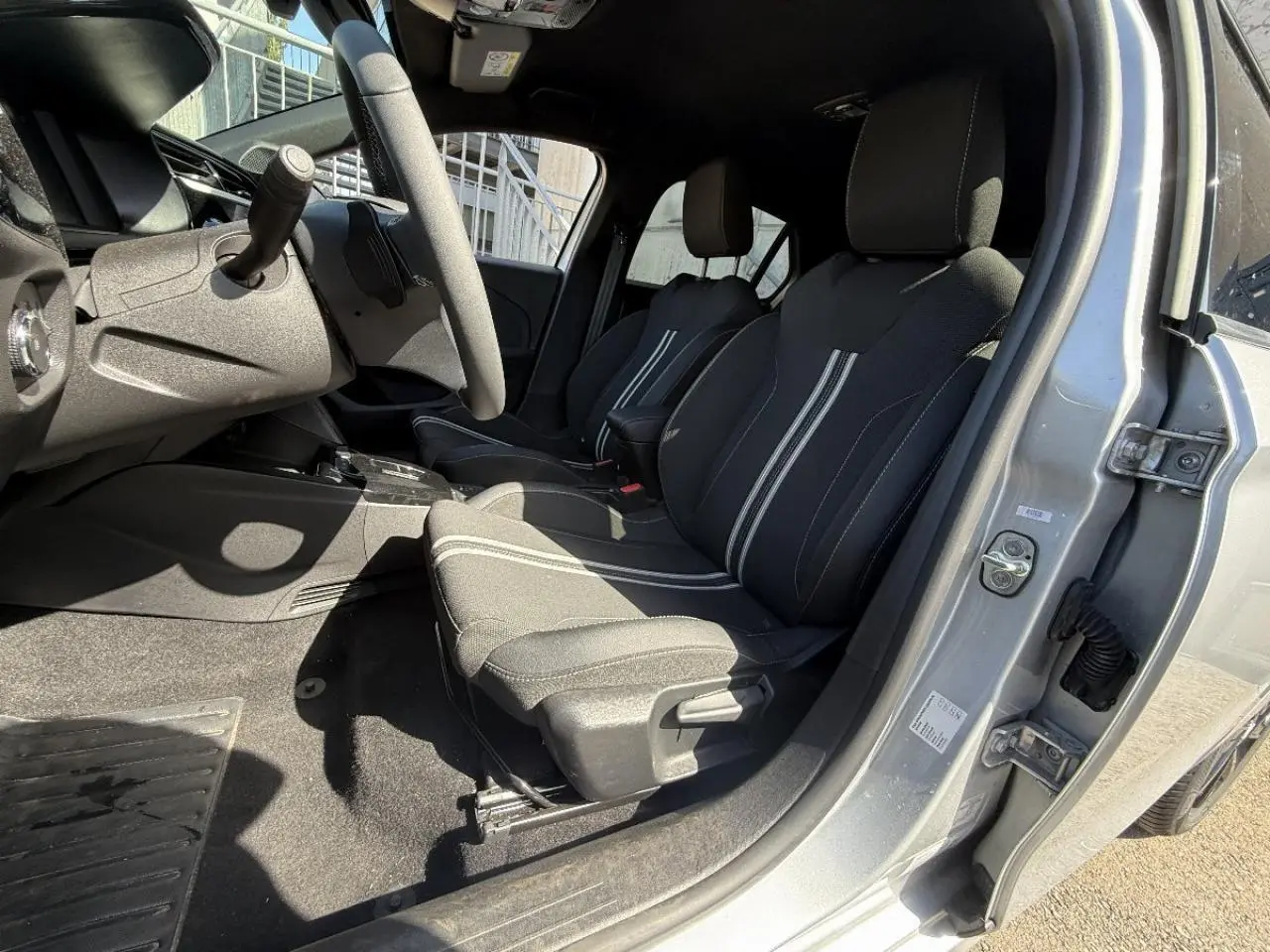 Vue intérieure côté conducteur de l’Opel Corsa gris kristall 2025, montrant les sièges avant avec surpiqûres blanches et volant.