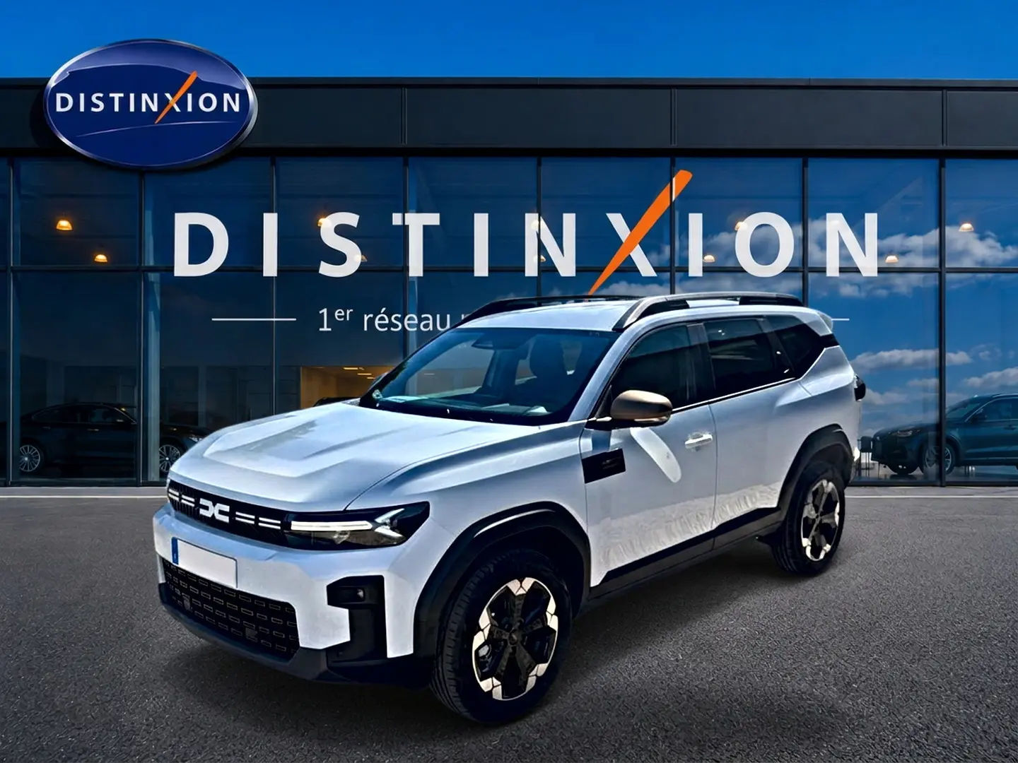 SUV Dacia Bigster blanc en 3/4 avant droit, avec jantes alu et barres de toit noires visibles.